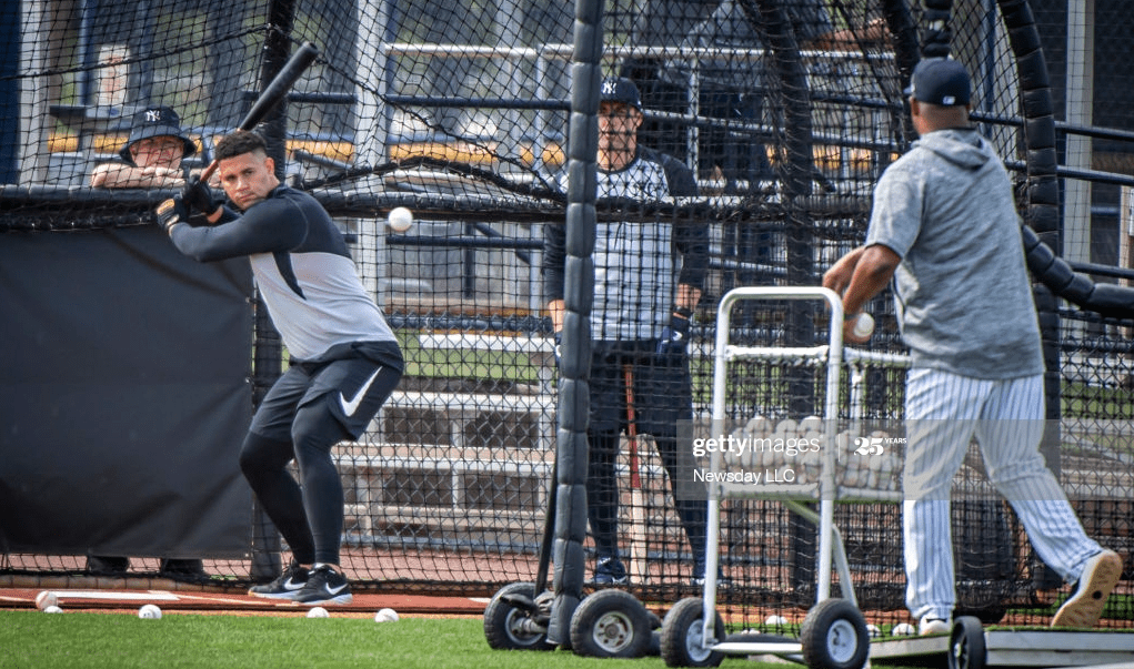 Baseball player preparing to swing with practice balls nearby and coaches observing