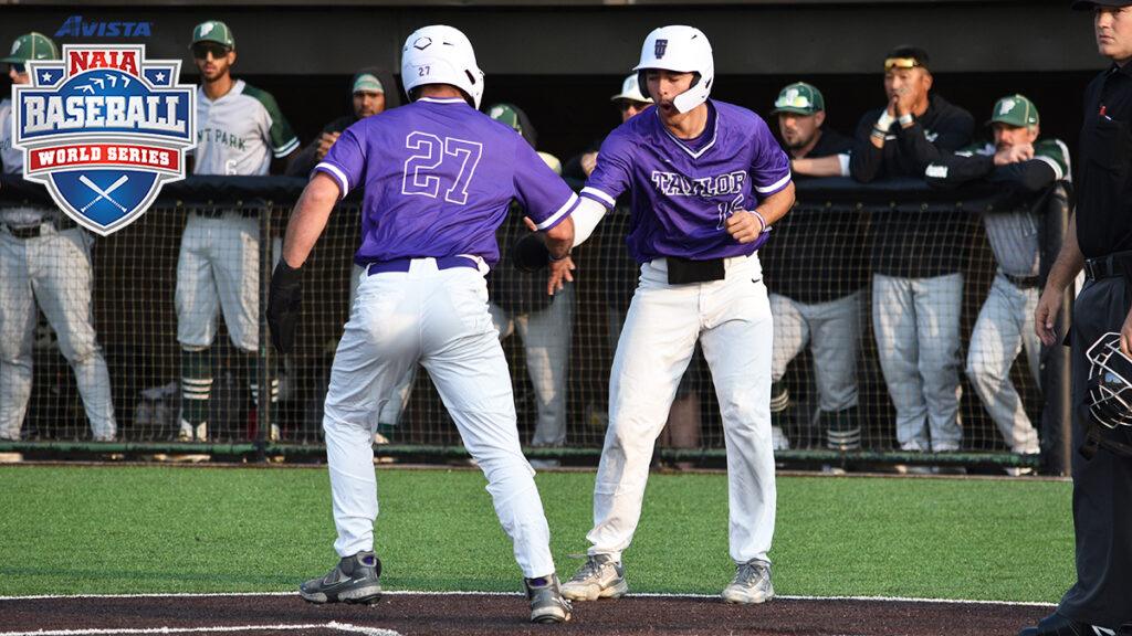 Two baseball players in purple uniforms high-fiving at home plate