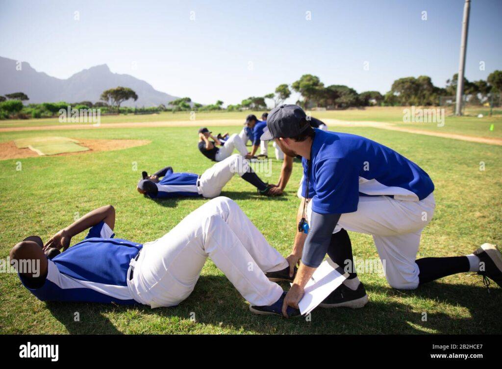 Baseball team members stretching on a grassy field with mountains in the background