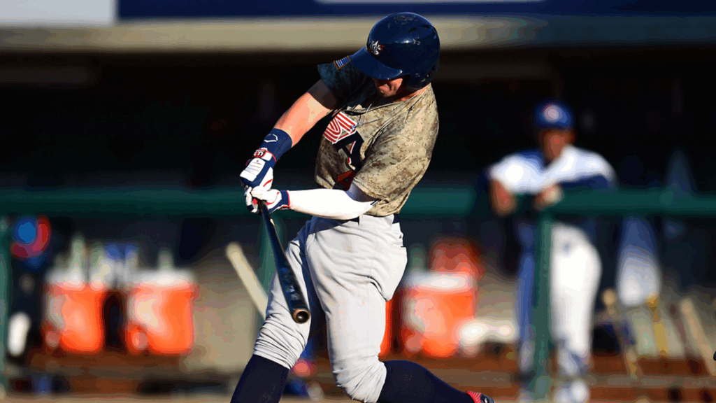 Athlete in camouflaged jersey swinging a baseball bat during practice