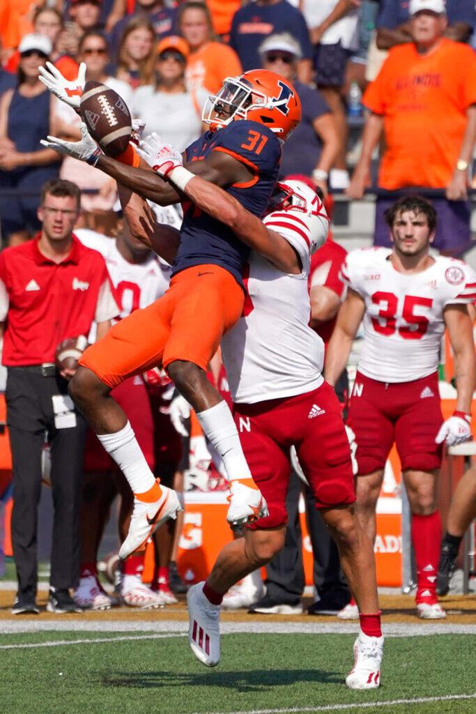 Player in orange and navy uniform catching a football while being defended