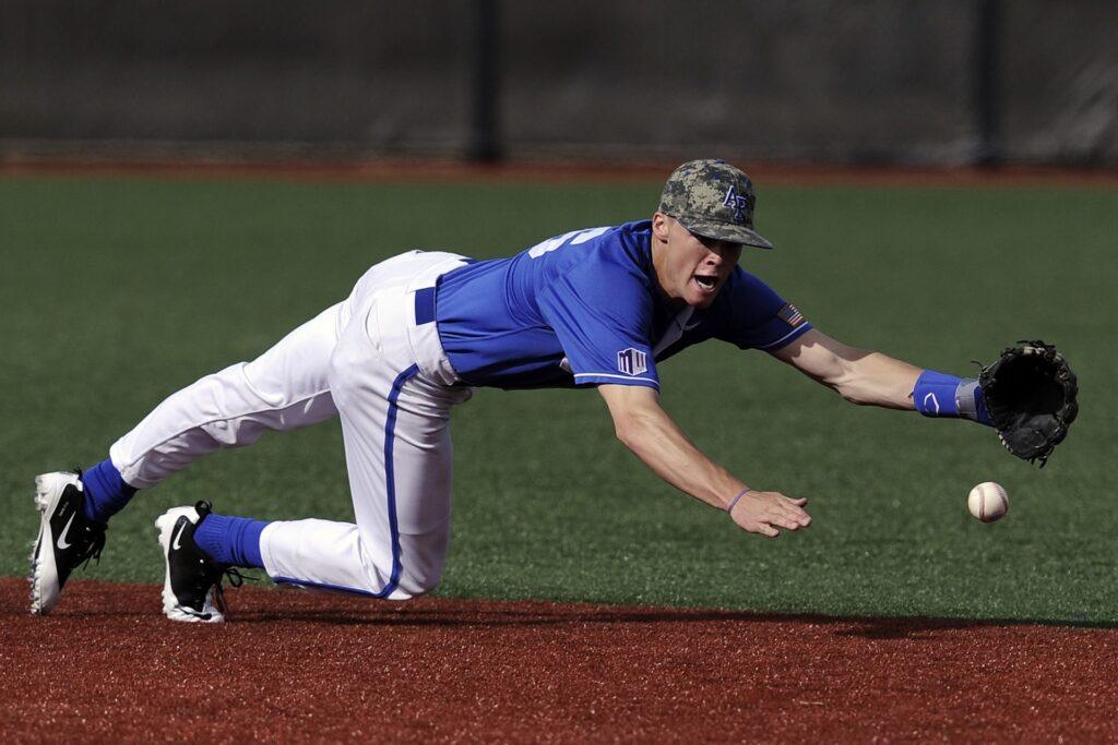 Baseball player in blue uniform diving to catch a ball on turf
