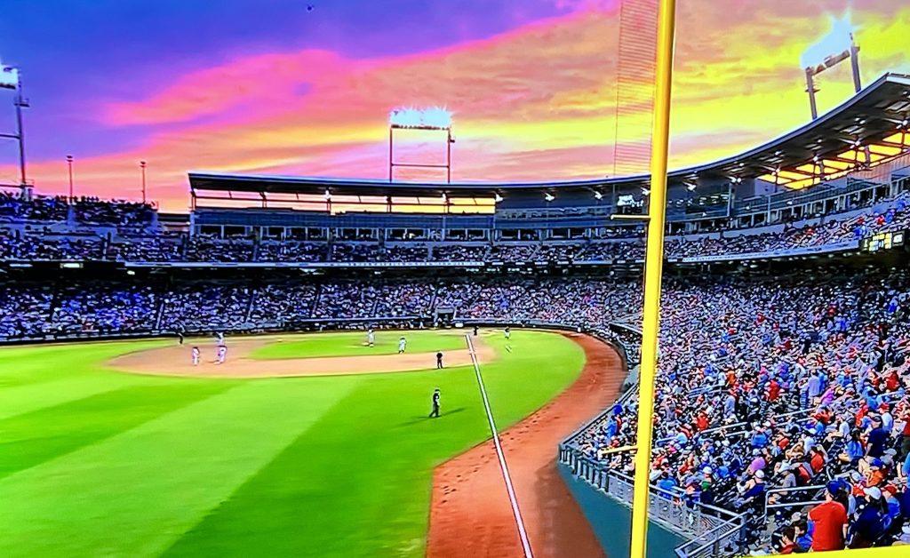 Crowd watches baseball game at sunset with vibrant sky colors