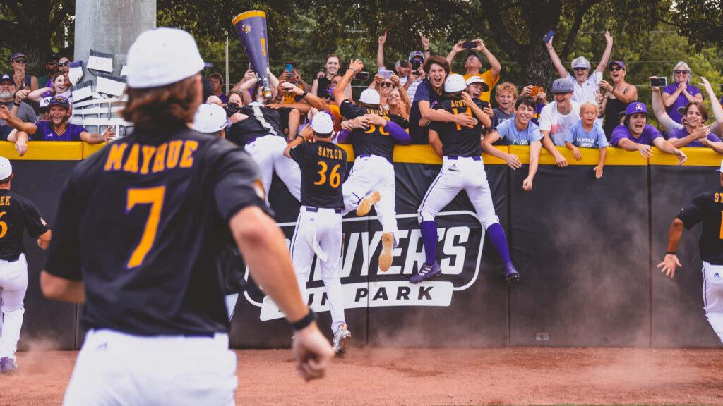 Baseball players celebrating by jumping over a wall with fans cheering in the background