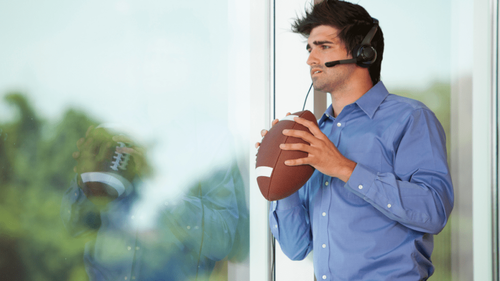 Man in a blue shirt holding a football while wearing a headset